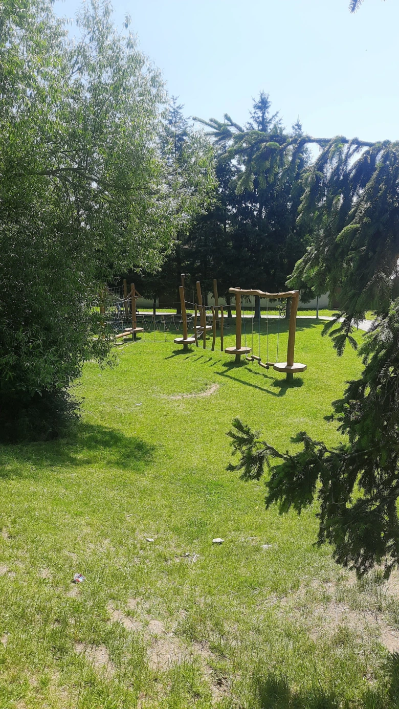 Venkovní hřiště s dřevěnými prvky na trávníku v přírodě.