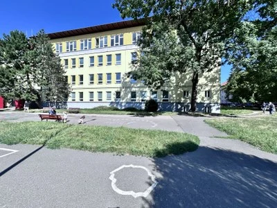 Žlutá školní budova s trávníkem a stromy v Ostravě.