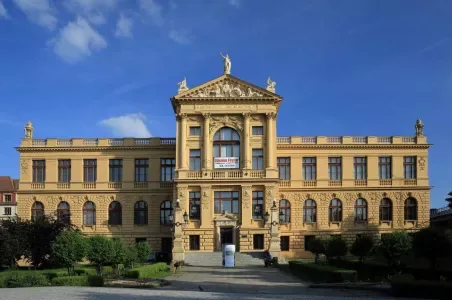 Velká historická budova muzea v Praze pod modrou oblohou.
