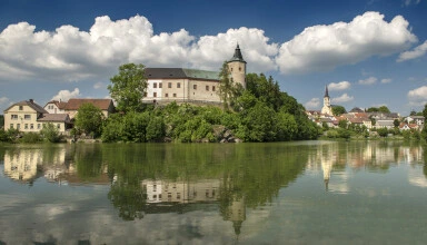 Zámek Kamenice nad Lipou s odrazem v řece pod oblohou.