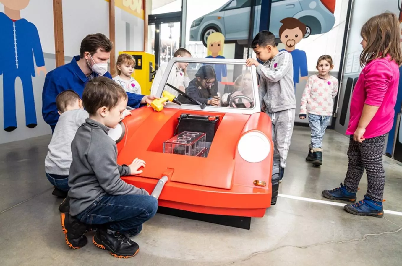Děti hrají s interaktivní červenou autem v muzeu.