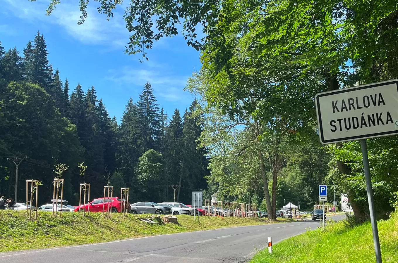 Vstup do Karlové Studánky s parkováním a lesním pozadím.